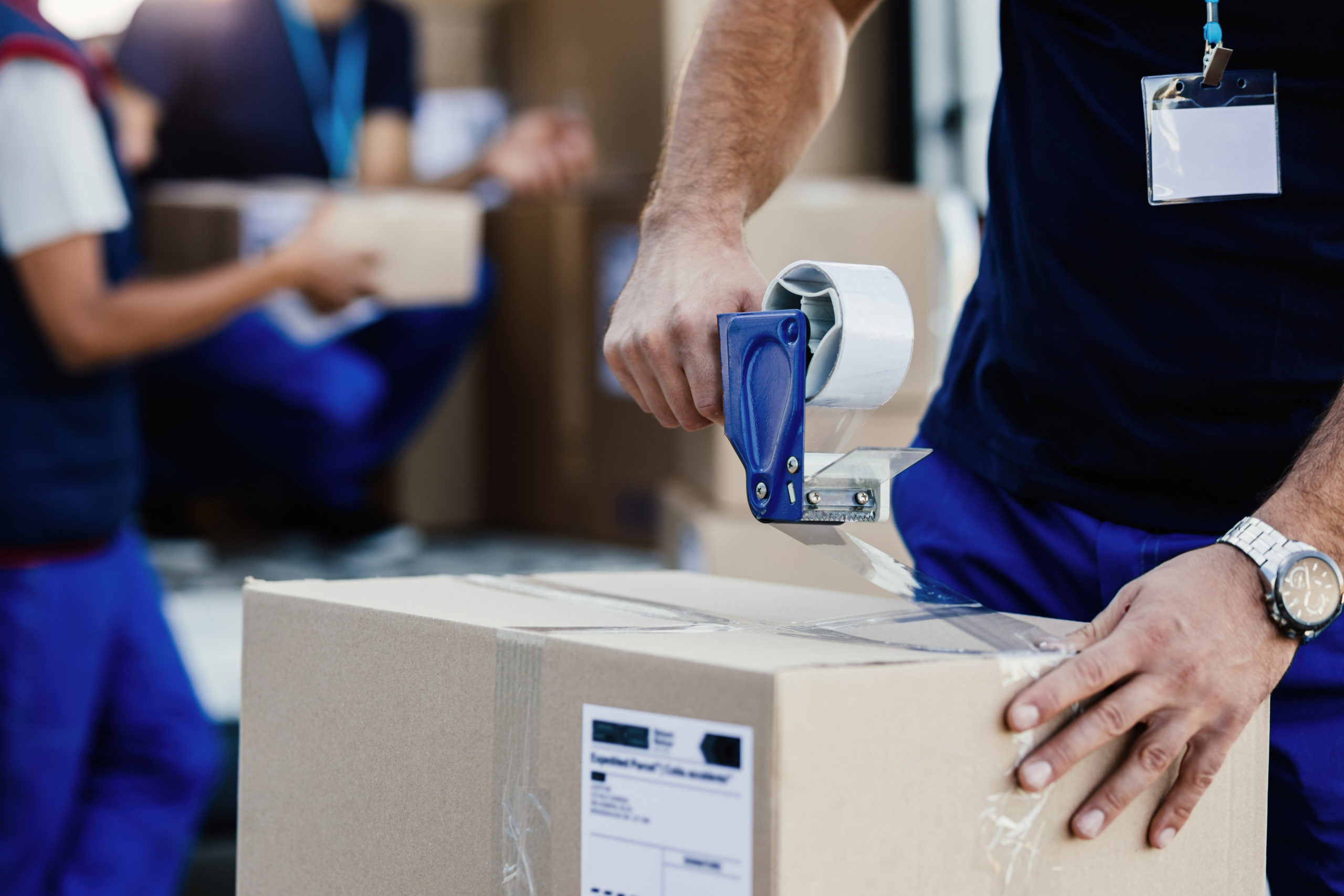 closeup-delivery-man-closing-carboard-box-with-tape-while-preparing-packages-shipment-scaled