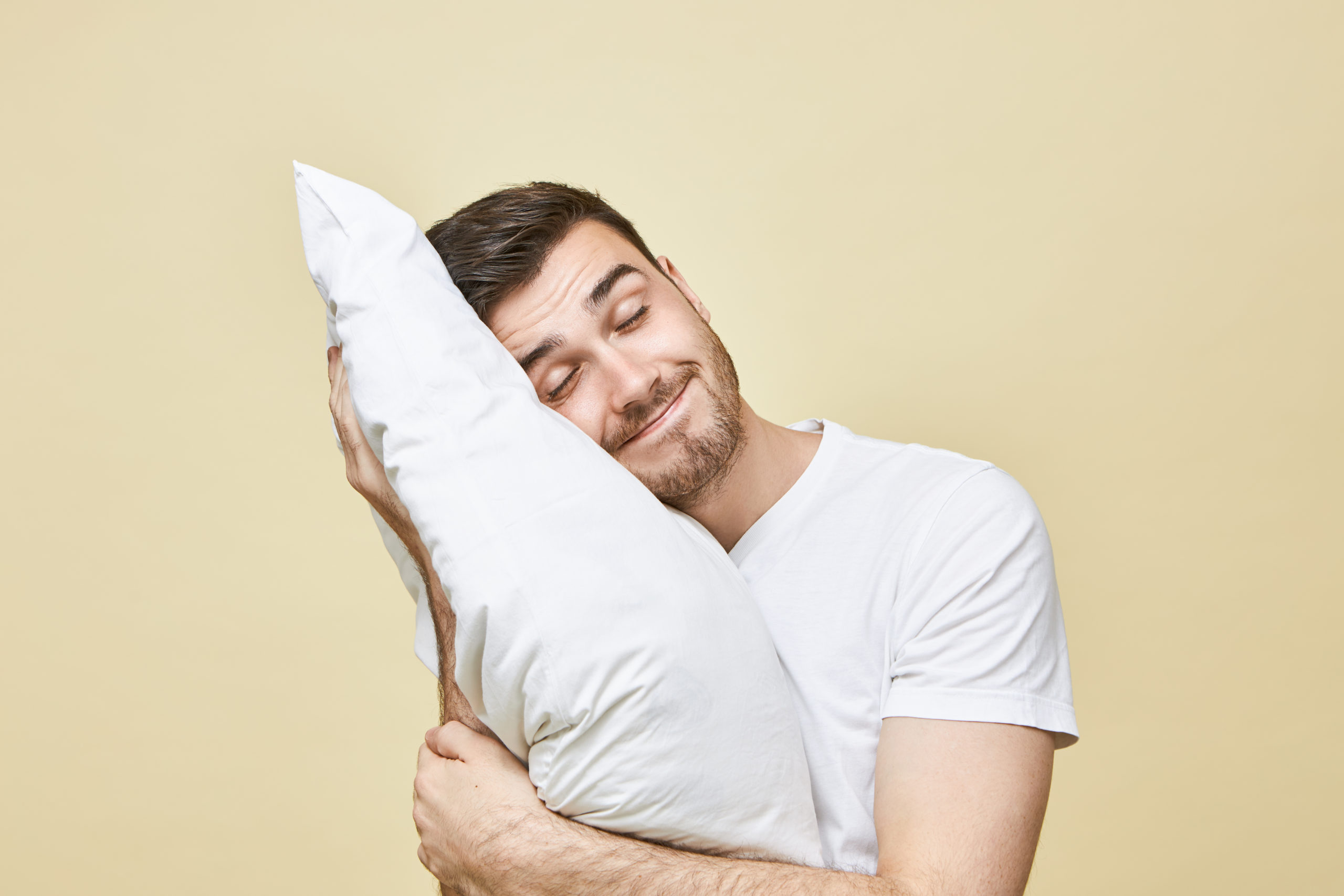 horizontal-image-handsome-cute-young-man-with-bristle-posing-with-head-white-soft-pillow-sleeping-peacefully-smiling-seeling-good-dream-attractive-guy-napping-after-hard-working-day-scaled