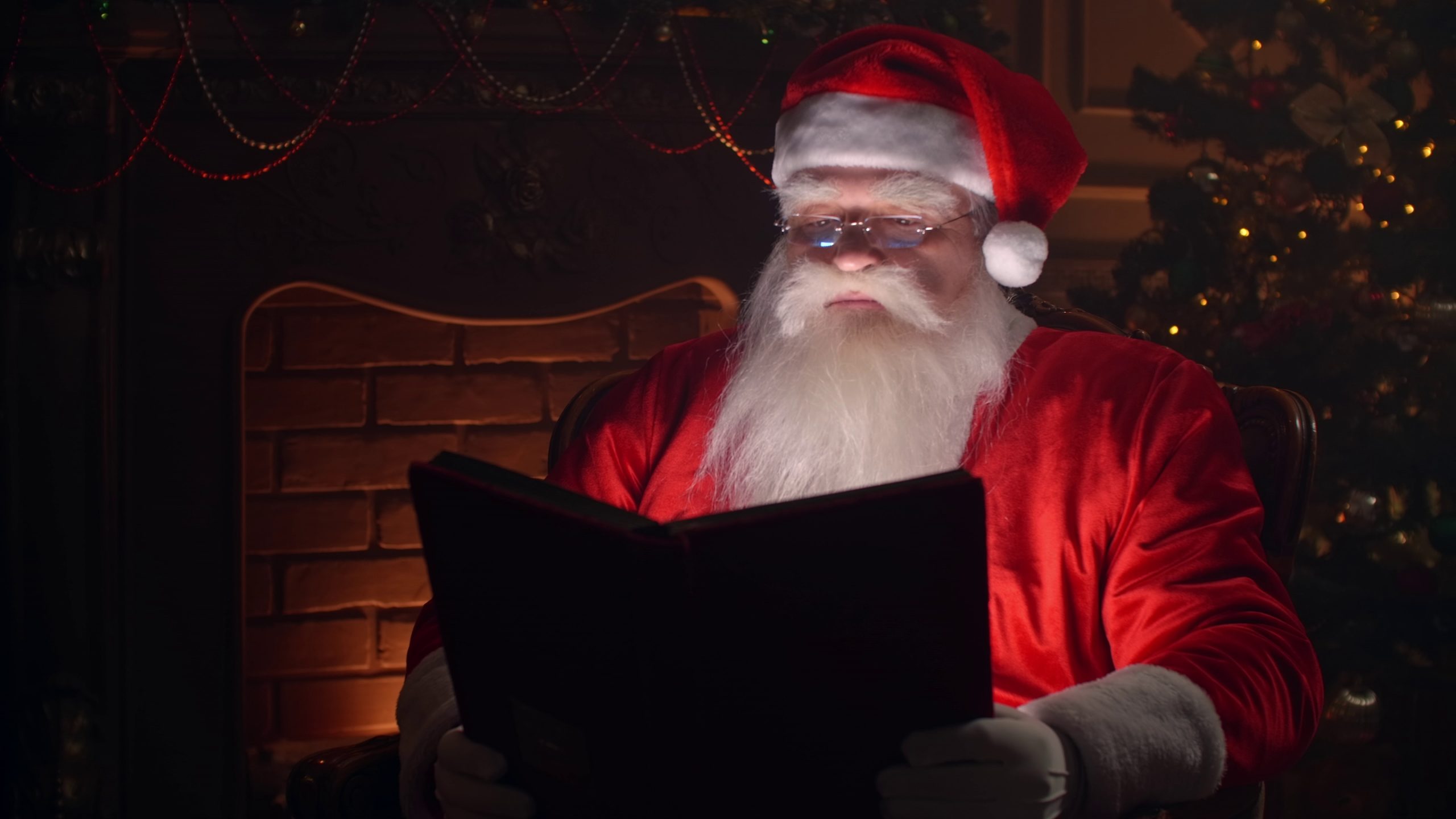bearded-senior-man-in-santa-clause-outfit-flipping-through-pages-of-book-with-red-cove-SBI-349452813-scaled